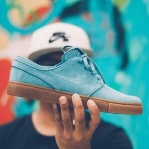 Close-up of a blue skate shoe held by a young adult against a colorful background.